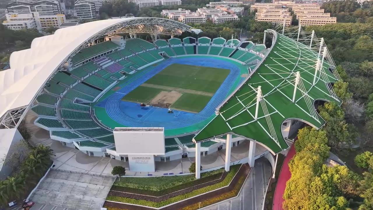 A UAV view of a stadium bowl and sports field surrounded by tiered seating and urban context.